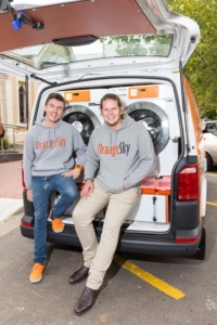 Nic and Lucas of Orange Sky Australia sitting at the bank of the van with the boot open